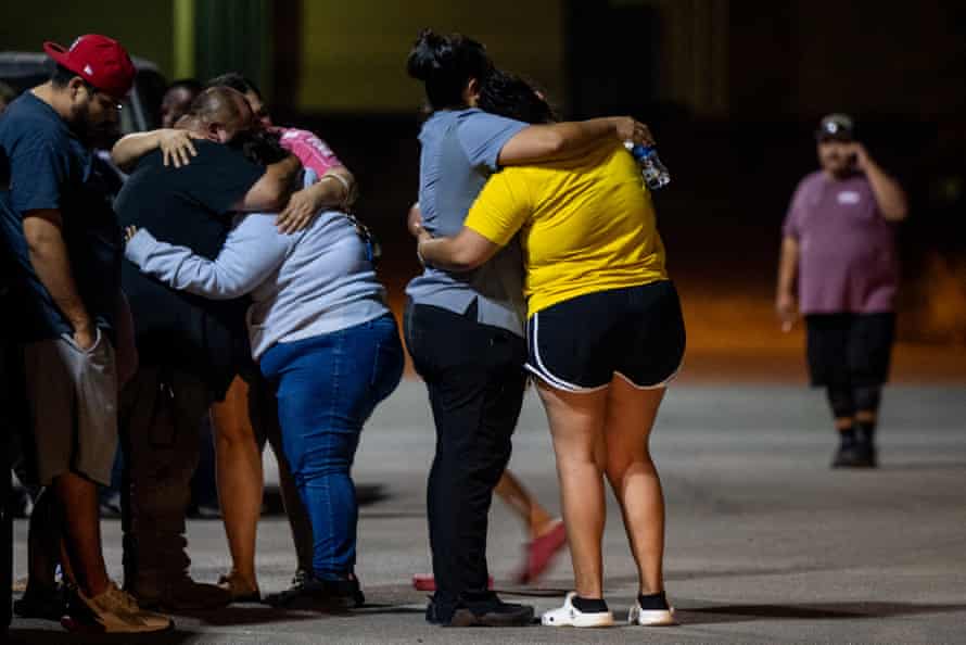 Families hug each other in a dark parking lot.