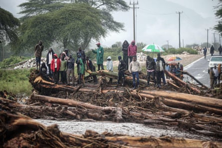 People stand on debris blocking a highway after River Muruny burst its bank following heavy rains in Parua village, in Kenya’s West Pokot county