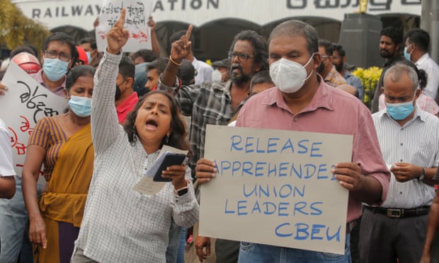 Protesters shout slogans. One has a sign saying “Release apprehended union leaders”