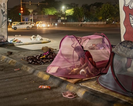 A woman crouches over a baby in a pink pop-up mosquito-netting tent