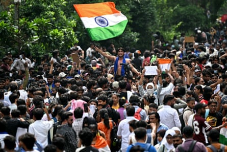 A group of people cheering, with one held aloft above the crowd waving the flag of India