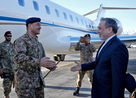 Asim Munir and Abbas Araghchi reach out to shake hands next to a plane