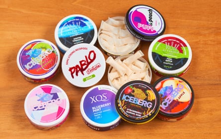 A collection of colourful, branded nicotine pouch tins, including two with their lids removed to reveal small white pouches inside.