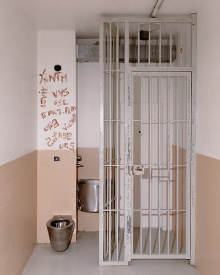 Words on a wall above a toilet next to a cage in a cell