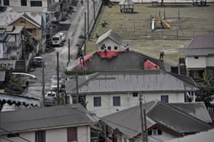 Volcanic ash covers St Vincent – in pictures 5 People clean volcanic ash from the red roof of a home in Wallilabou.