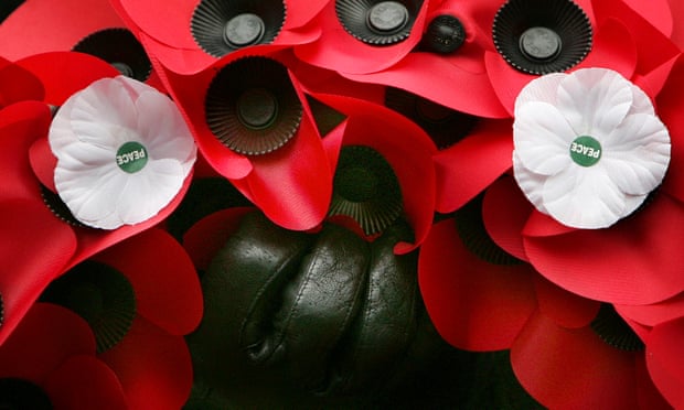 A wreath of red poppies, with white poppies of peace, is held at a remembrance service.