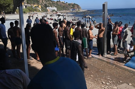 Dozens of people who crossed from Morocco line up to use the public showers on El Trampolín beach in Ceuta, where hundreds have been sheltering for more than a week.