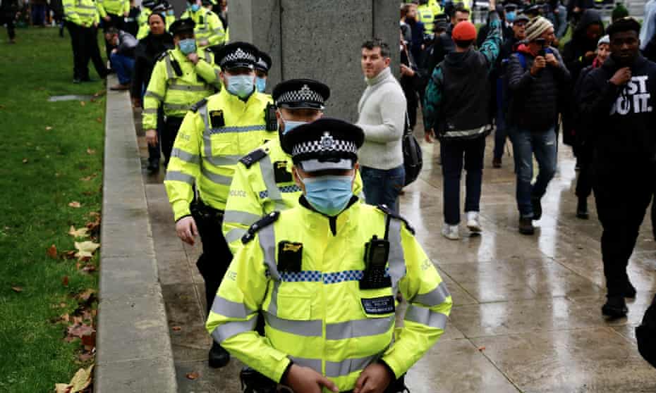 Police officers in face masks stand guard during a protest against meeting in the British Parliament.