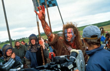 Mel Gibson in costume surrounded by people in soldier costumes, with a director with a camera.