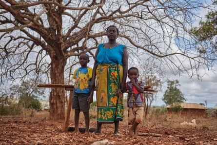 A black woman stands with a child either side of her, holding hands, next to a tree