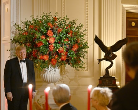 Trump in a tuxedo near an eagle with wings outspread on a plinth
