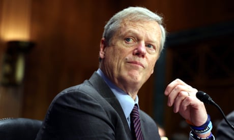 Middle-aged a man at a microphone and in suit and tie looks up