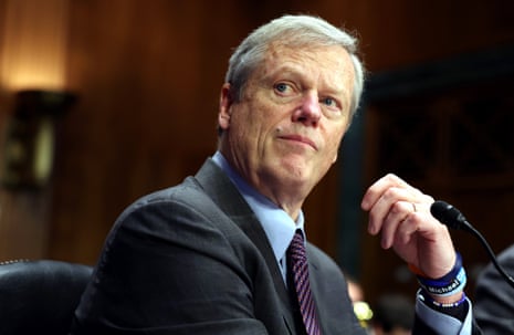 Middle-aged a man at a microphone and in suit and tie looks up