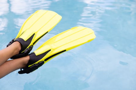A pair of legs hanging over blue water, with yellow fins of their feet