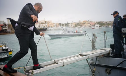 Cleverly clambers on to a Guardia di Finanza police boat in Lampedusa port.