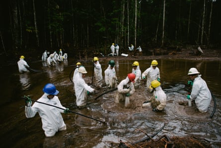 Workers in white hazmat suits and hard hats clear spilled crude oil from a river in the Amazon jungle, Peru.