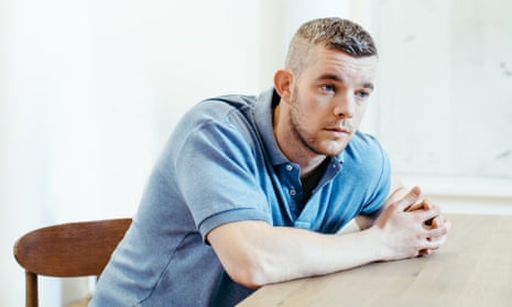 Russell Tovey in a pale blue polo shirt, sitting at a table, leaning forwards