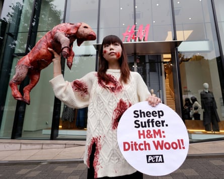 A person wearing a bloodied jumper holding up a model of a bloodied sheep outside an H&M store