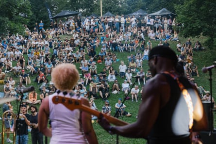 Live musicians on stage pictured from behind with large festival outdoor audience