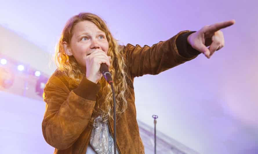 Kate Tempest on stage, holding a microphone in one hand and pointing ahead with the other