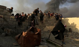 Crowds rush to grab humanitarian packages, as smoke rises from a burning oil refinery in Qayyarah, south of Mosul.