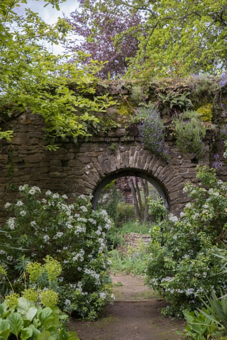 A view through into Munstead Wood’s summer garden from the herbaceous border, with cream, lilac and violet blooms surrounding a weathered stone archway.