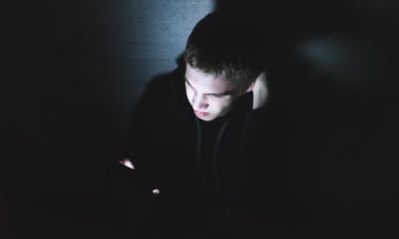 A person in a darkened room whose face is illuminated by the light from a phone screen