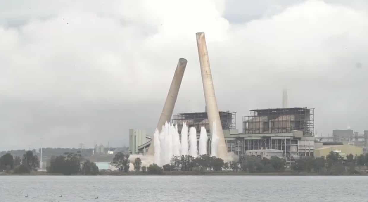 Two chimneys collapse in the skyline in front of a power station