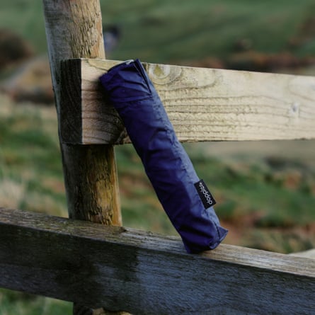 Folded-up compact umbrella in its sleeve leaning against the rails of a fence