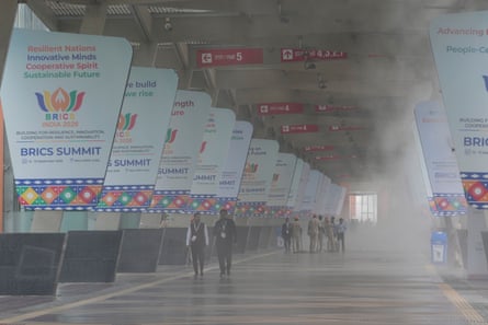 People walk through mist underneath a concrete overpass, with signs proclaiming the Brics Summit hanging from each pillar.