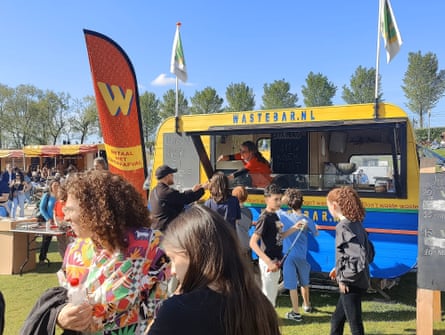 A yellow truck with a queue of people in front of it.