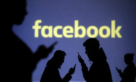Silhouettes of mobile users  next to a screen projection of Facebook logo