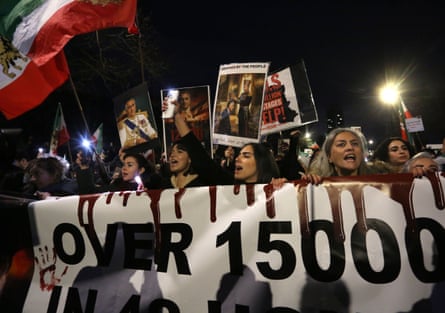 A crown of people march behind a banner, holding placards and an Iranian flag.