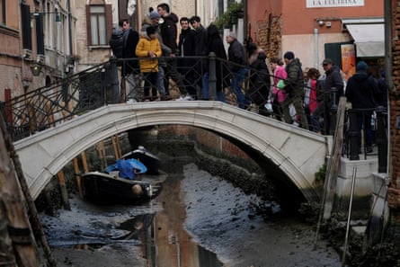 Tourists cross a bridge over a noticeably empty canal during a severe low tide in Venice, Italy.