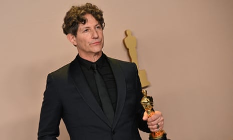 man in a black suit holding a gold oscar statuette