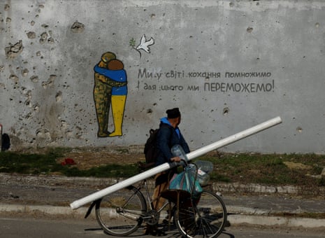 A man cycles past graffiti on a wall of a building covered with traces of bullets and shrapnel in the recently liberated town of Kupiansk, Ukraine.