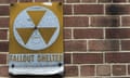 A nuclear fallout shelter sign hangs on a brick wall