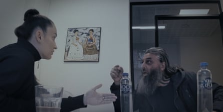 A women with her hair in a tight bun talks intensely to a man with a full beard. Both are gesticulating.