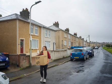 A girl carries a box of belongings down a rainy residential street