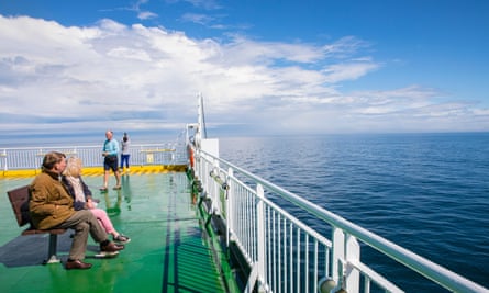 Passengers sit onboard the ship’s deck, looking out to sea.