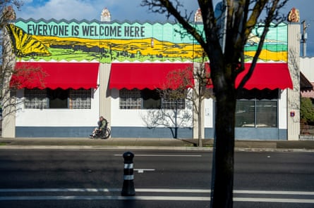 Brightly colored one-story building, with white walls, red awnings, and mural on top that says Everyone Is Welcome Here.