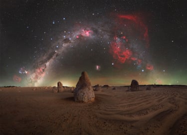 A calm, windless night in the Pinnacles desert, as the main limestone pillar aligns almost perfectly with the South Celestial Pole, anchoring the image beneath the rotating sky. To the right, the faint but unmistakable red glow of the Gum Nebula, a vast supernova remnant, adds depth and scale to the scene
