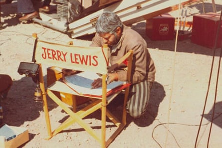 Lewis kneels on the ground, reading from a folder using his director's chair as a table