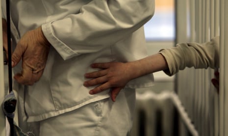 A patient tries to reach a nurse's uniform through cot bars