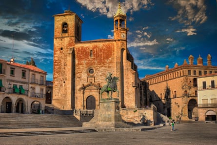 A sunny city square with old yellow sandstone buildings and a statue of a man on a horse