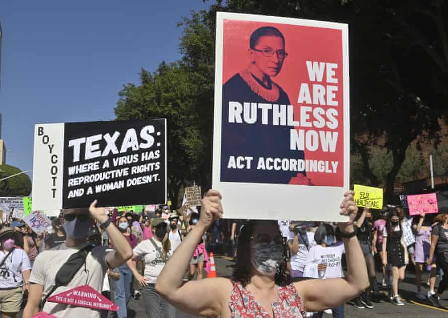 People hold signs at a march in Los Angeles in October. One sign reads "Texas: where a virus has reproductive rights and a woman doesn't" and the other says "We are Ruthless now. Act accordingly" over a background of former supreme court justice Ruth Bader Ginsberg.