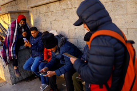 group of people looking at phones against a wall