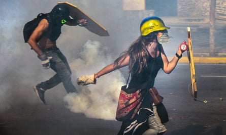 Venezuelan opposition activists clash with the riot police in Caracas. Many now wear gas masks and construction helmets.