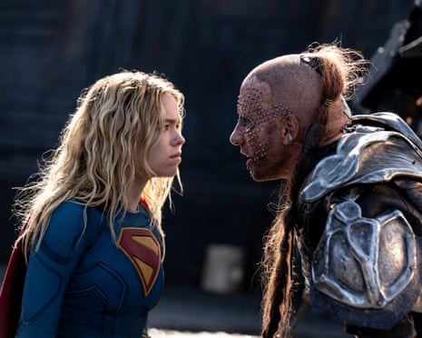 Supergirl faces a person in armor with studded face makeup and wild hair