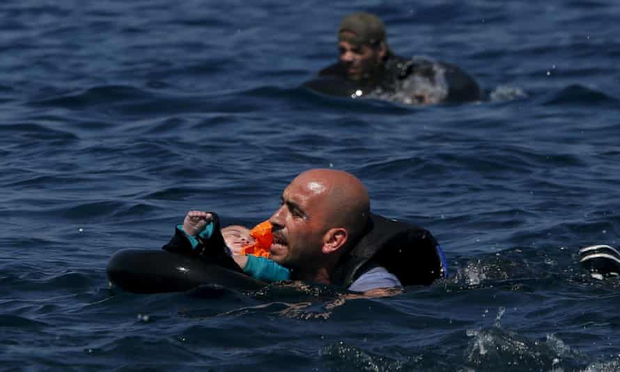 A Syrian refugee holding a baby in a lifetube swims towards the shore after their dinghy deflated 100m off the Greek island of Lesbos at the weekend.